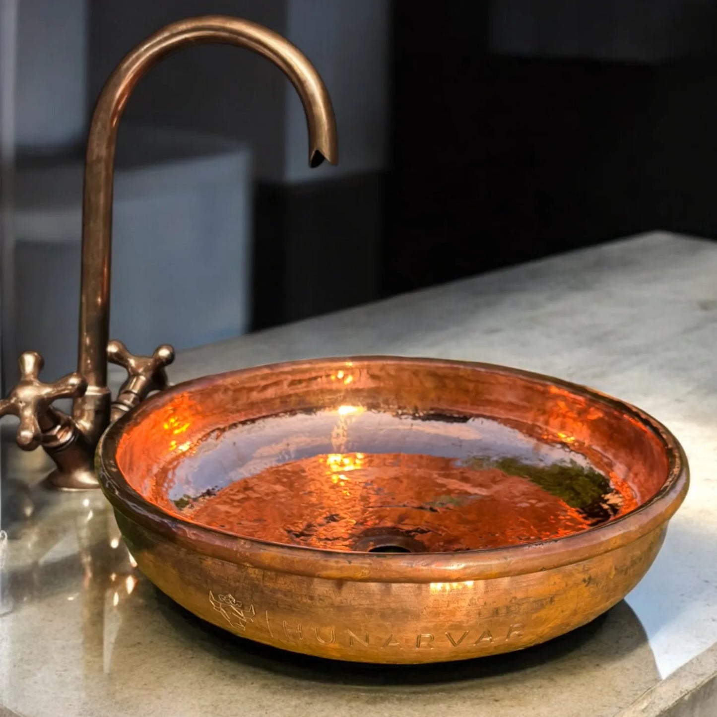 Edles Kupferwaschbecken mit glänzender, gehämmerter Oberfläche und passendem Kupfer-Wasserhahn auf heller Steinplatte im modernen Bad