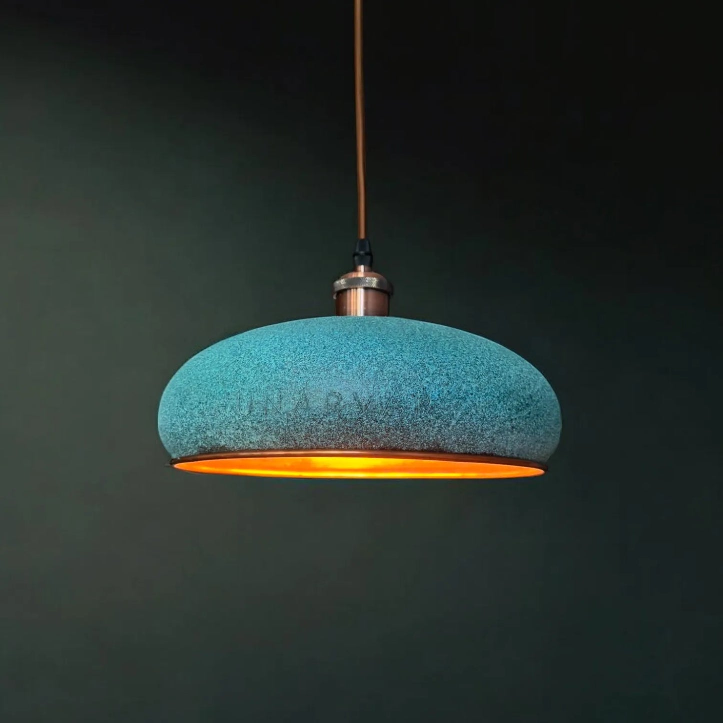 Türkise selbst patinierte, handgefertigte Kupfer Pendelleuchte mit warmer Lichtabstrahlung, hängend vor dunklem Hintergrund.