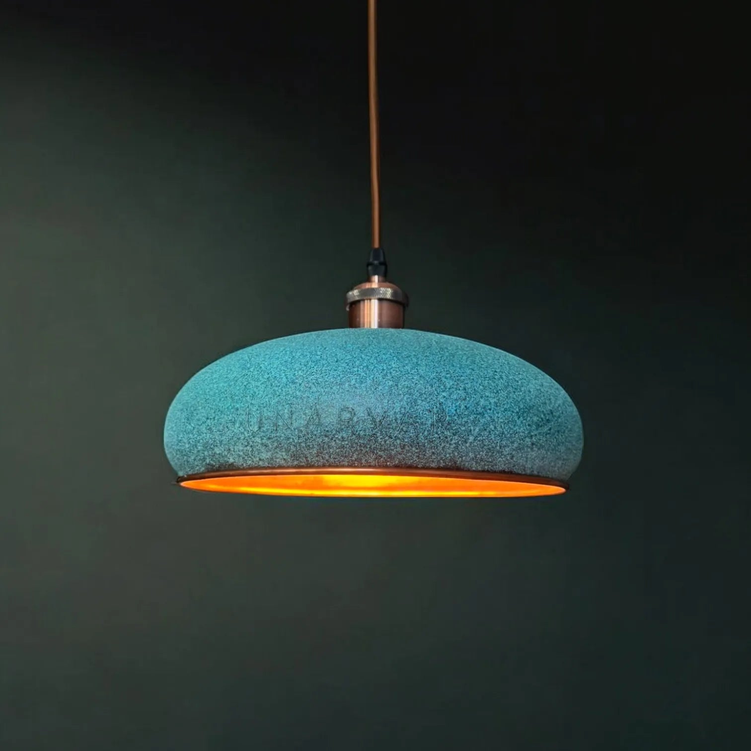 Türkise selbst patinierte, handgefertigte Kupfer Pendelleuchte mit warmer Lichtabstrahlung, hängend vor dunklem Hintergrund.