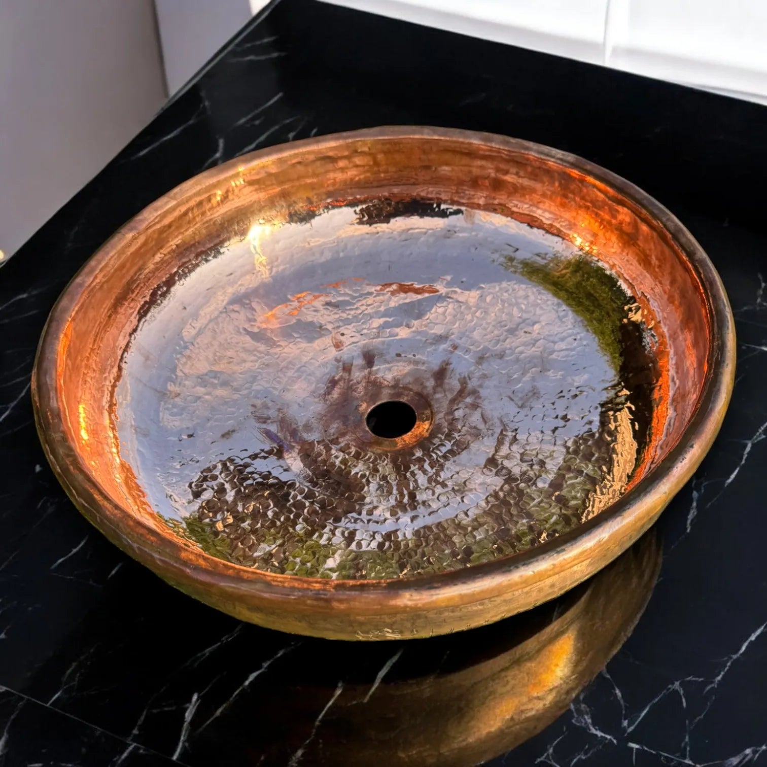 Handgefertigtes Kupferwaschbecken mit glänzender, gehämmerter Oberfläche auf schwarzer Marmorplatte, luxuriöses Bad-Design